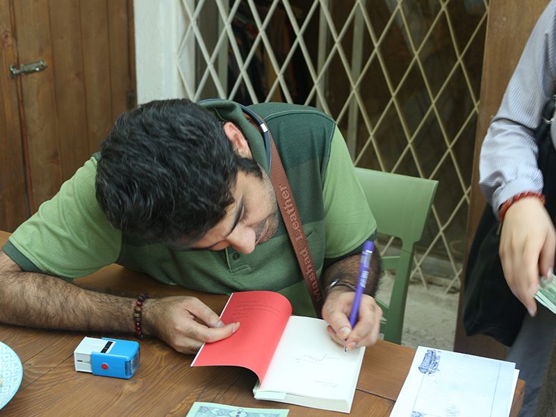 حسام الدین مطهری در حال امضای کتاب در میهمانی دورهمی رمان تذکره اندوهگینان